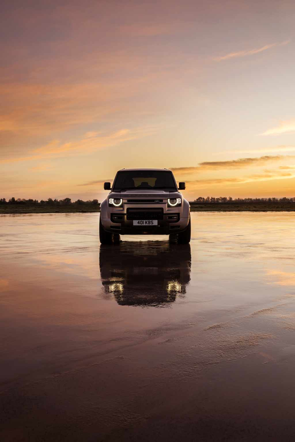 Land Rover Defender at golden sunset reflected on a still lake